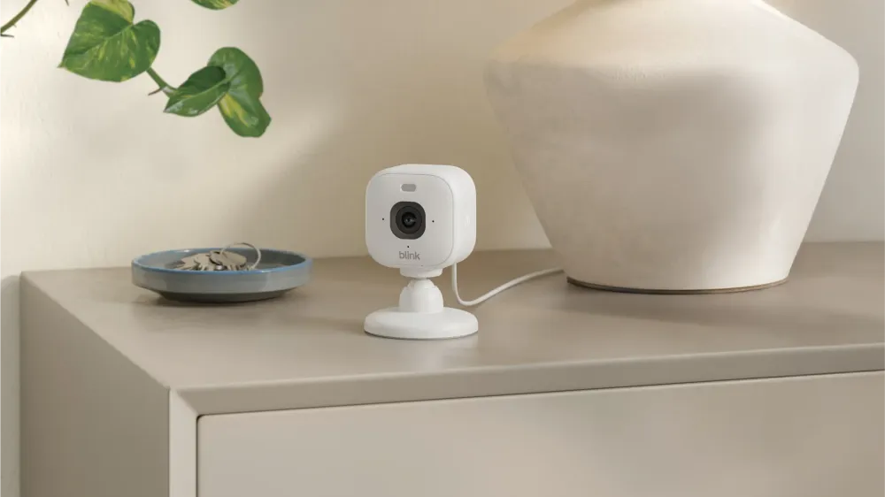A Blink Mini 2K camera on a dresser in a family living room, next to a bowl of keys