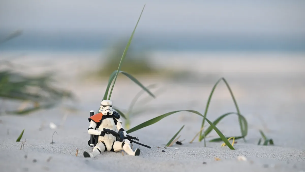 Sandtrooper figure seated in a dune hollow among sea grass blades