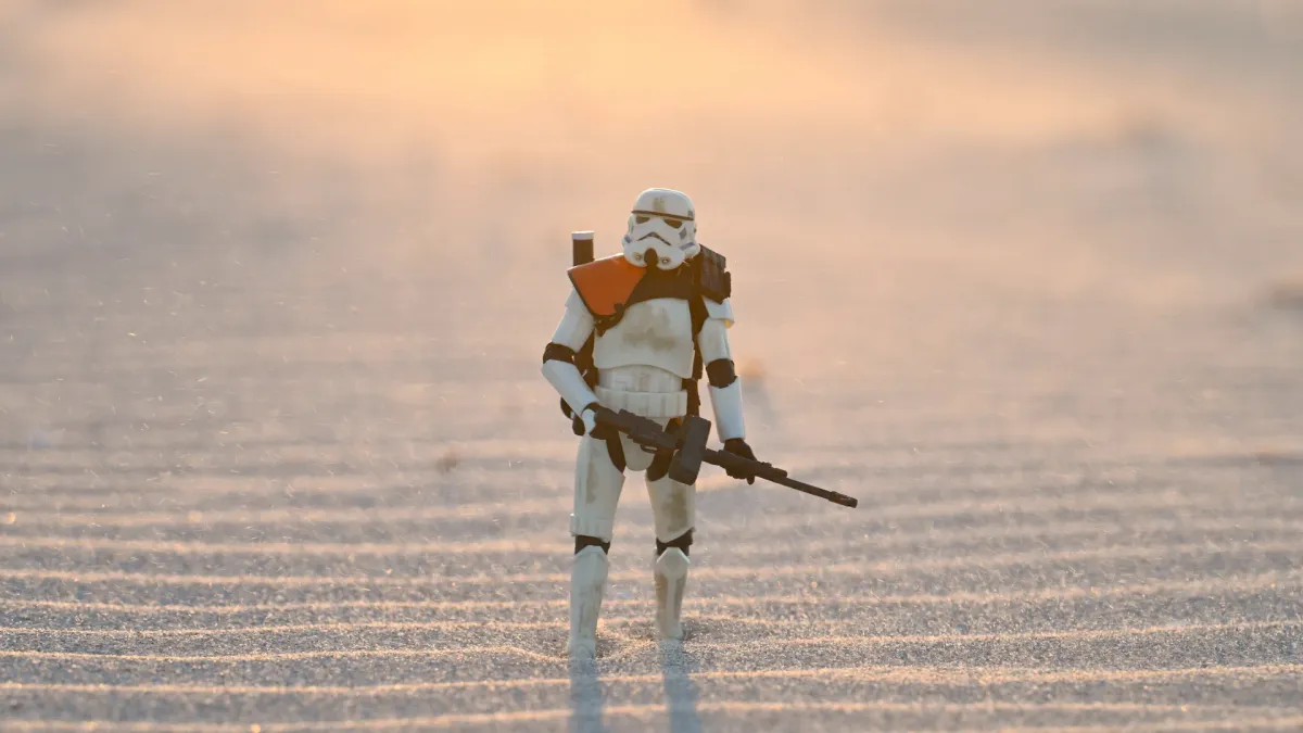 Sandtrooper walking across wave-rippled sand with windblown dust catching the warm golden sunlight