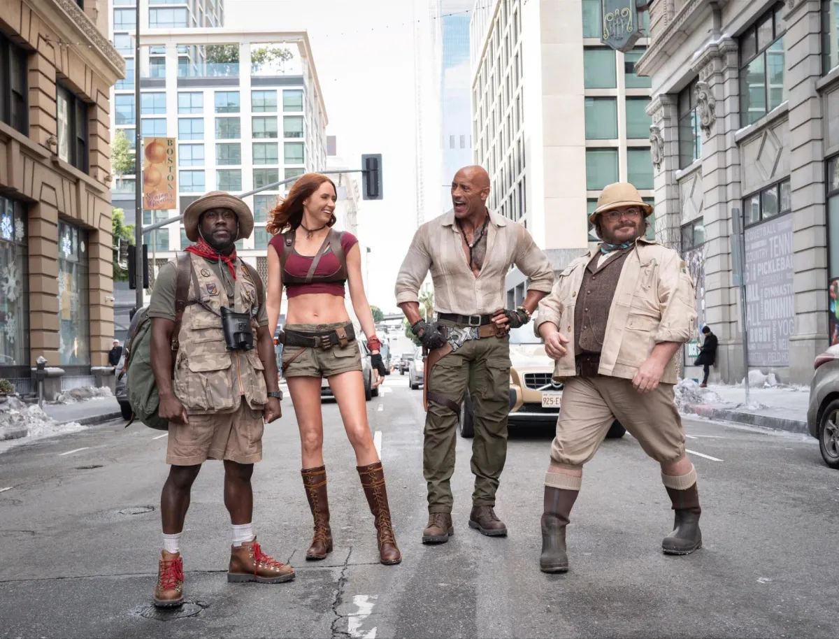 Dwayne Johnson, Karen Gillan, Kevin Hart and Jack Black in their game-avatar costumes standing on a real-world city street in Jumanji: Open World