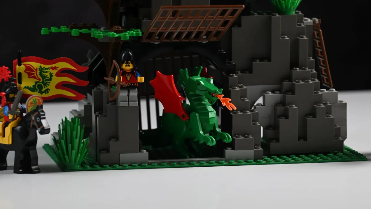 Close-up of the green fire-breathing dragon from LEGO Dark Dragon's Den (6076), posed outside its barred cage with a Dragon Knight archer standing guard above