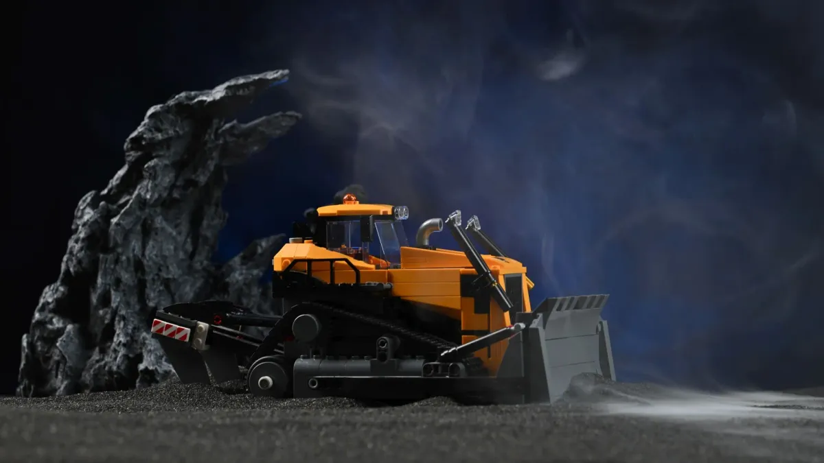 The LEGO City Yellow Bulldozer (60466) with its blade raised, photographed on a construction-site diorama with smoke and rock props