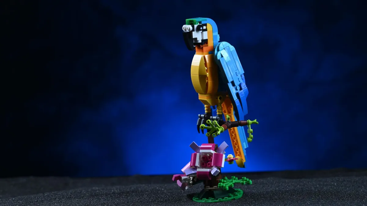 The LEGO Creator Exotic Parrot (31136) build perched on its tree branch, wings and tail spread, next to pink flower details