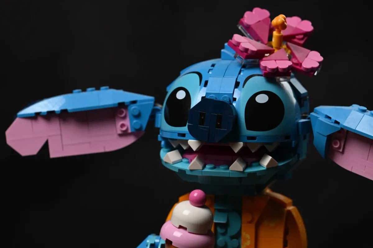 Close-up of the LEGO Disney Stitch (43249) face, showing the toothy grin, printed eyes, poseable ear hinge and the ice-cream cone accessory in his claw