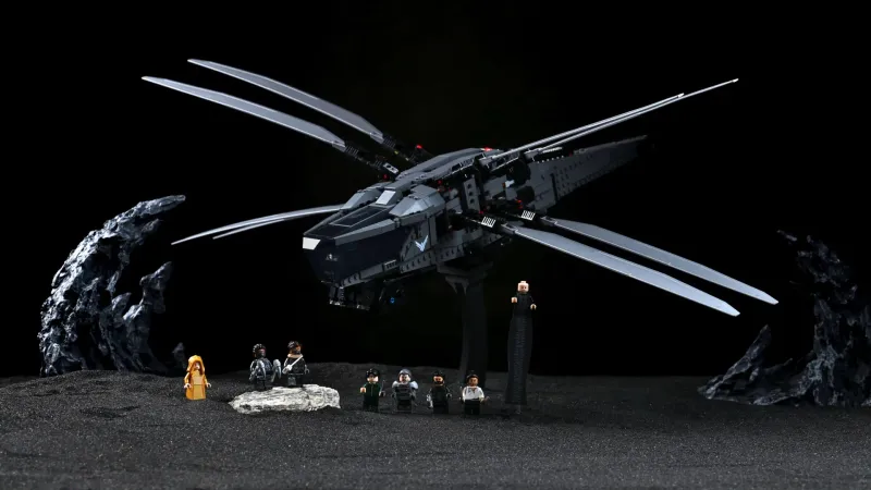 The built LEGO Icons Dune Atreides Royal Ornithopter (10327) with wings fully extended, displayed on black sand with all eight minifigures lined up beneath it