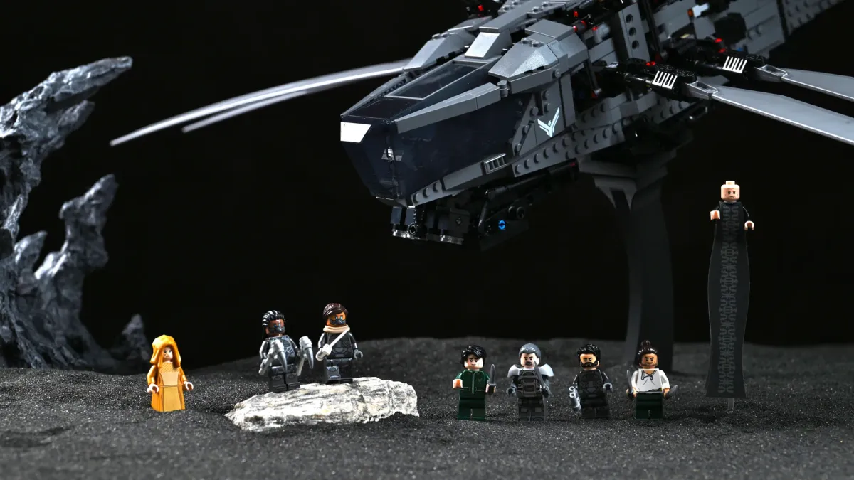All eight LEGO Dune Ornithopter minifigures lined up on black sand beneath the model: Paul Atreides, Lady Jessica, Duke Leto, Chani, Duncan Idaho, Gurney Halleck, Liet-Kynes, and Baron Harkonnen