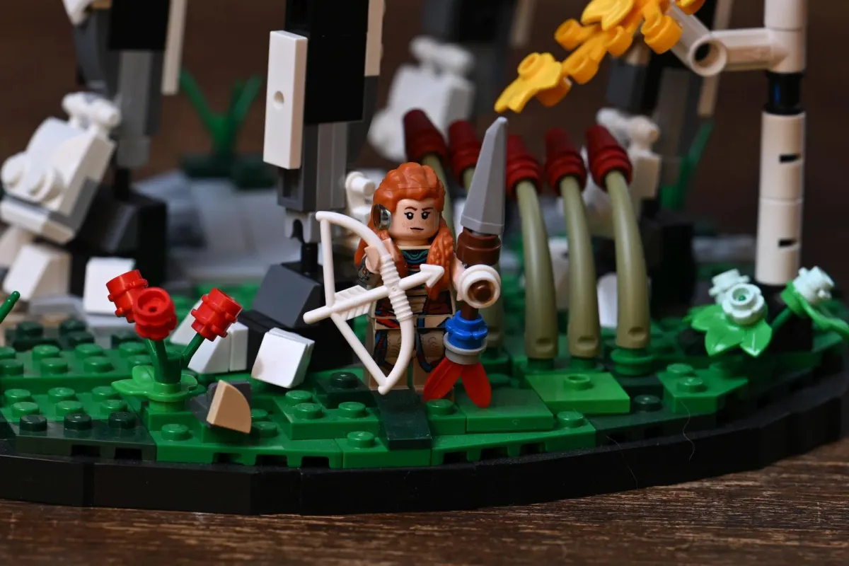 Close-up of the LEGO Aloy minifigure with her red hair, bow and spear, standing among the base's foliage and flowers
