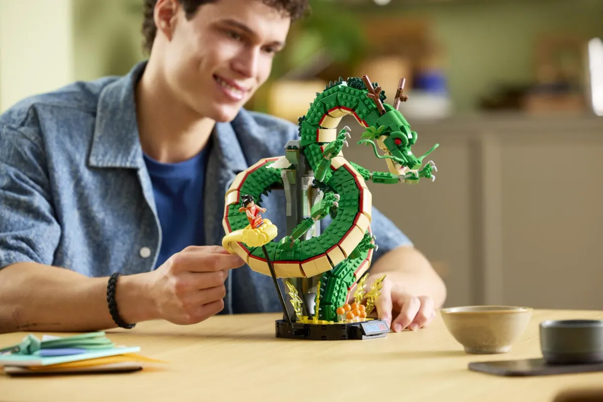 An adult fan adjusting the Kid Goku figure on the fully built LEGO Shenron set on a wooden table, showing scale