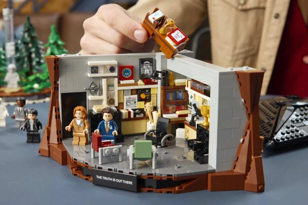 Close-up of Mulder's basement office inside the LEGO Ideas The X-Files set 21369, with the I Want to Believe poster on the wall and a hand placing a filing detail into the room