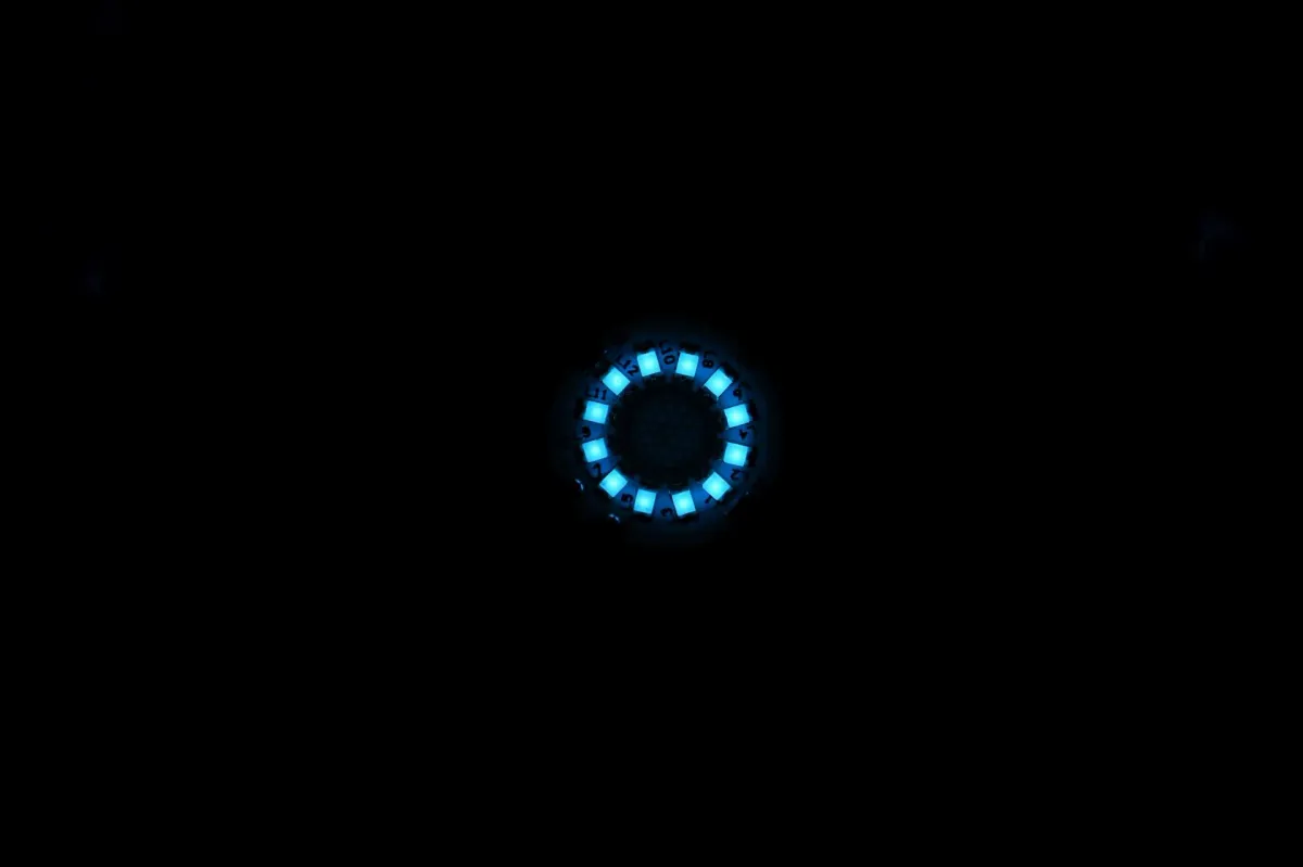 Close-up macro shot of the BriksMax LED arc reactor ring glowing ice blue in complete darkness