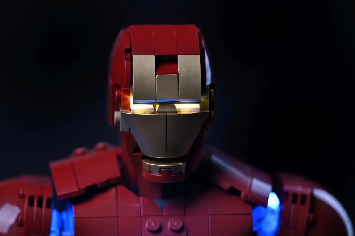 Close-up of the LEGO Iron Man Mark 3 helmet with the eyes glowing warm gold through the faceplate, lit by the BriksMax light kit