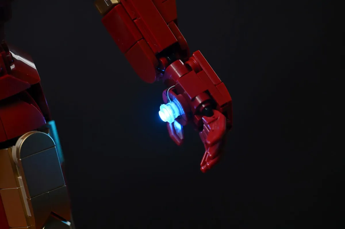 Macro shot of the LEGO Iron Man Mark 3 hand with the palm repulsor LED glowing blue against a black background