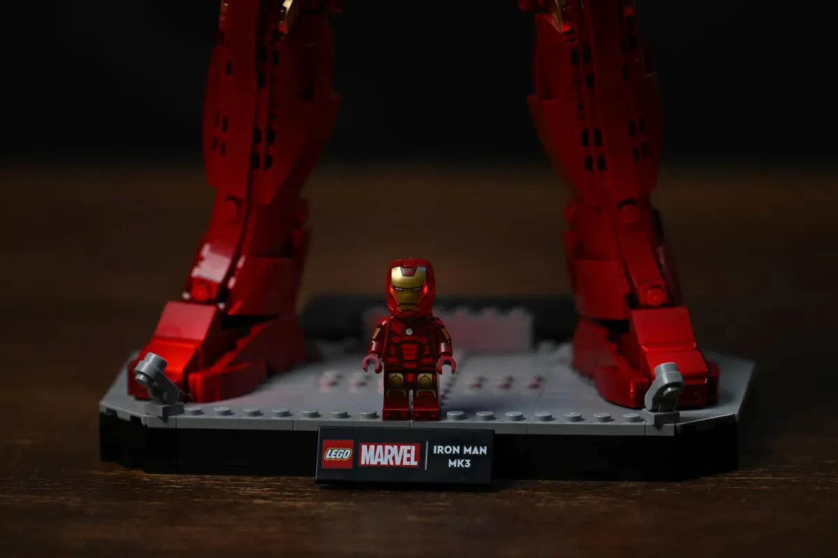 The exclusive Iron Man Mark 3 minifigure standing on the display base between the feet of the large LEGO figure, next to the LEGO Marvel Iron Man MK3 name plaque