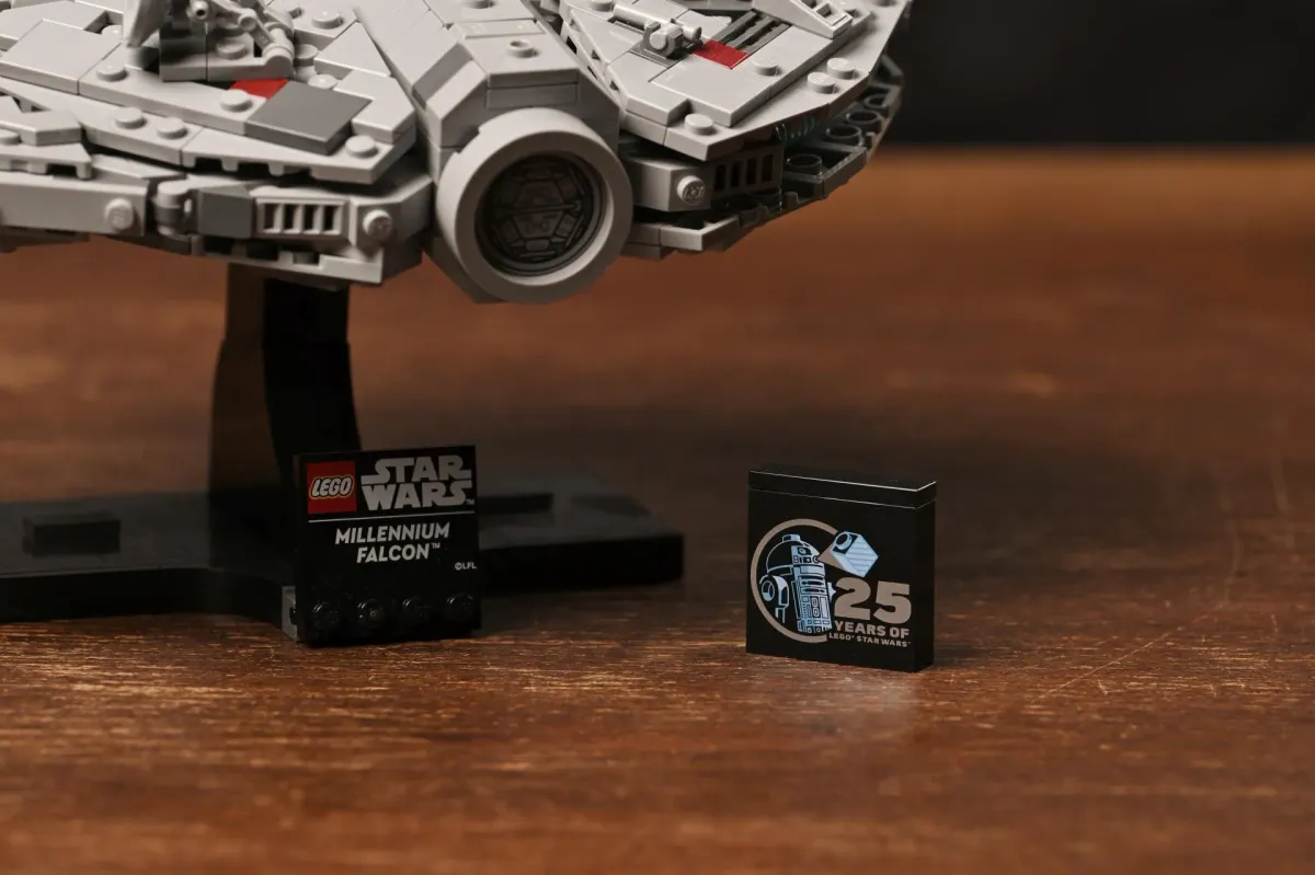 Close-up of the LEGO Millennium Falcon's display stand, the Millennium Falcon nameplate and the 25th-anniversary R2-D2 tile on a wooden table