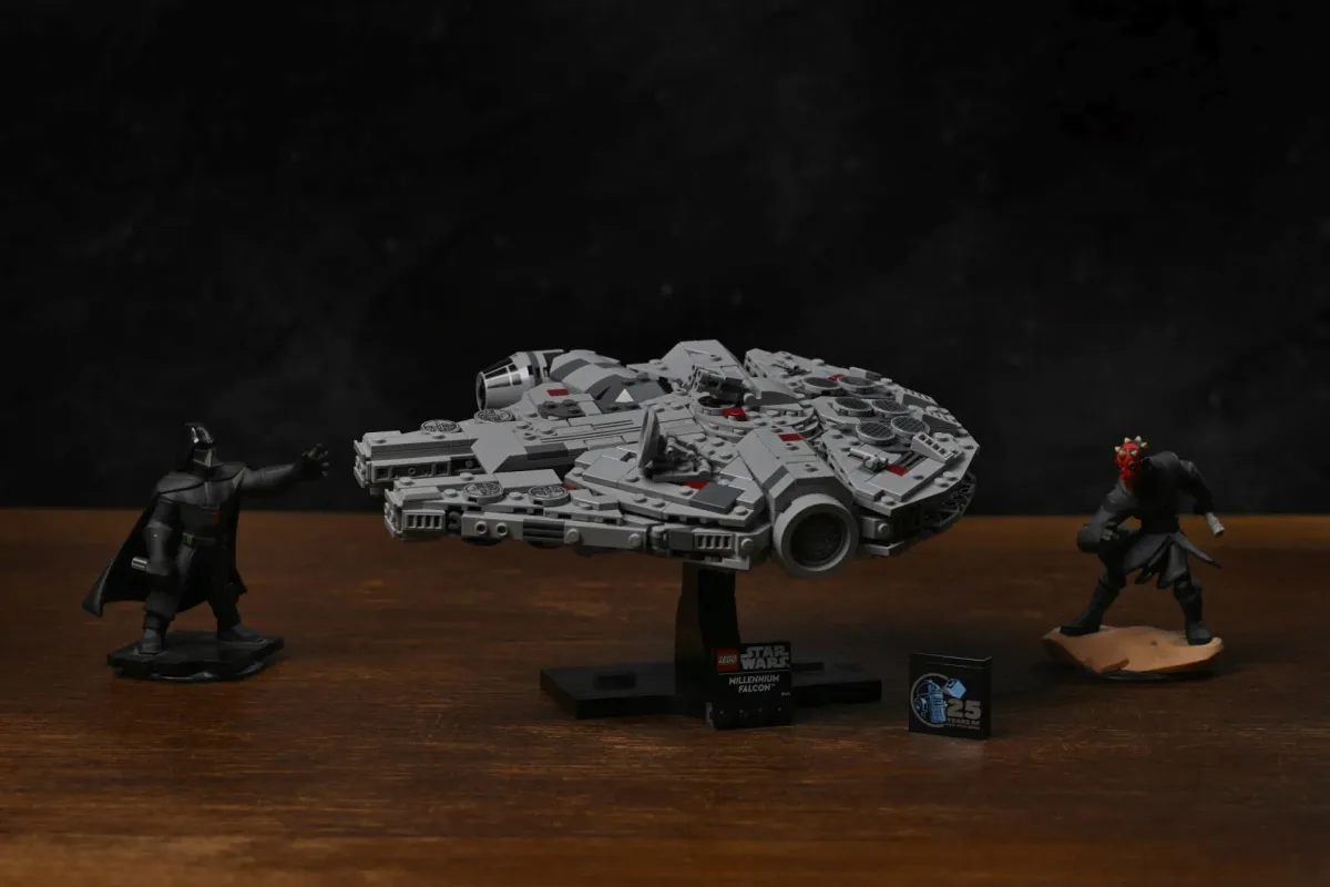 The LEGO Millennium Falcon (75375) on its stand between two Star Wars figures, Darth Vader and Darth Maul, on a wooden table