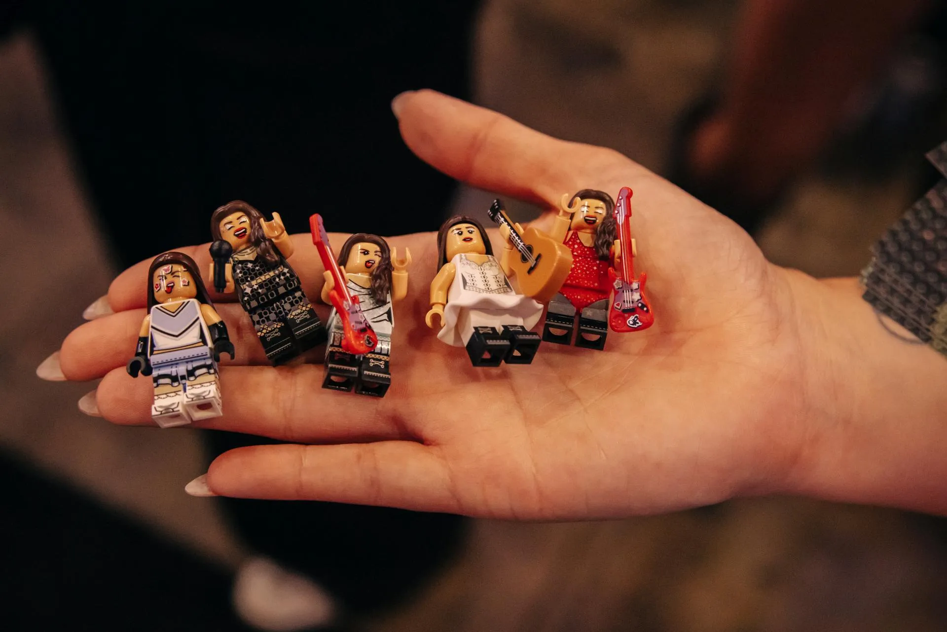 Five LEGO Editions Olivia Rodrigo minifigures, each in a different tour or festival outfit and holding a tiny guitar, resting in an open hand
