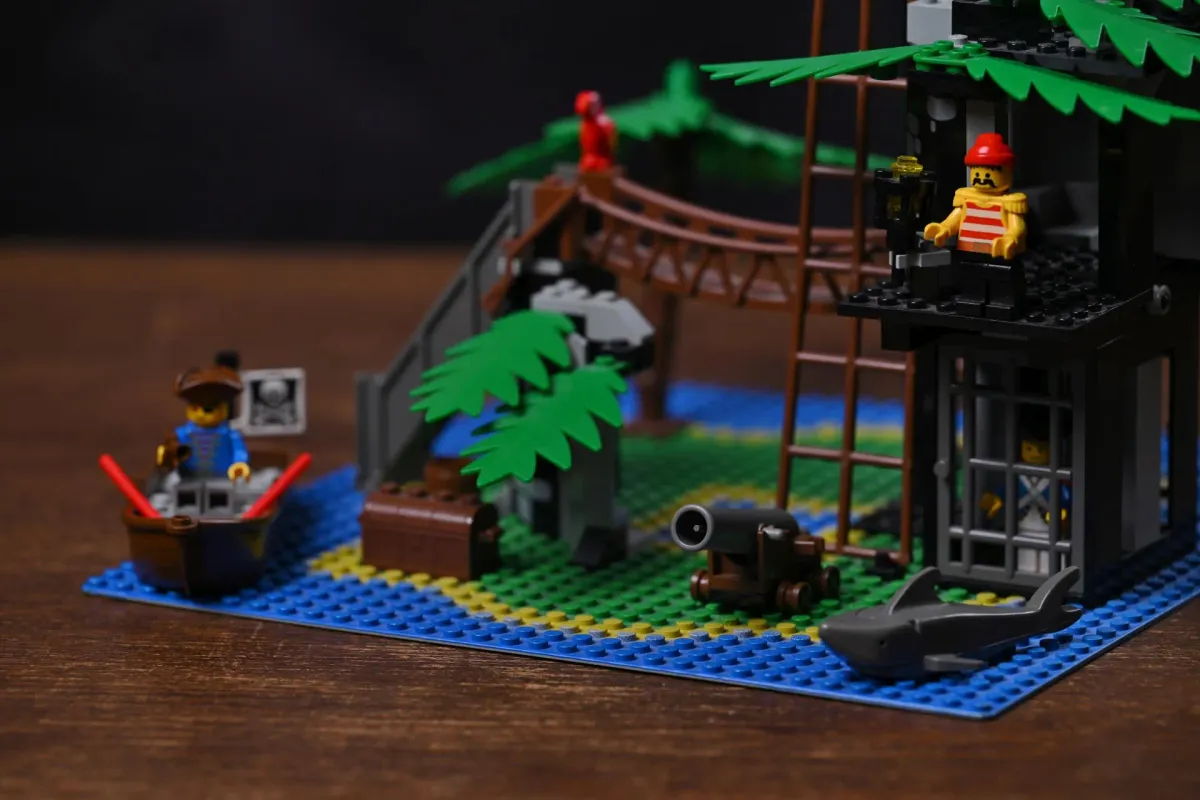 Close-up of the LEGO Pirates Forbidden Island (6270) island baseplate showing the rope bridge, palm trees, dungeon cell with prisoner, cannon, and shark