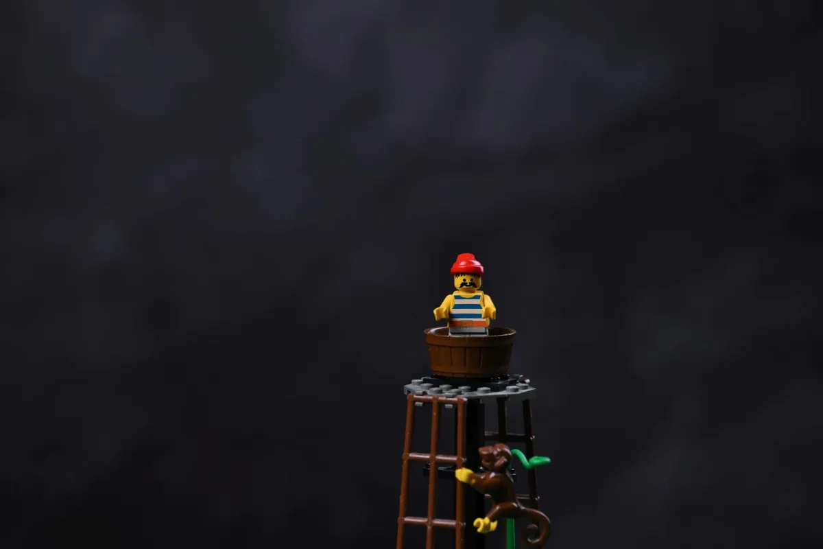 Close-up of a LEGO pirate minifigure standing in the barrel lookout post at the top of the Forbidden Island (6270) watchtower, with a monkey climbing the ladder below