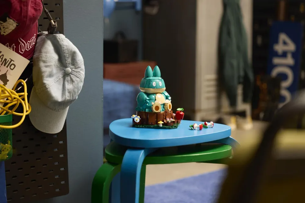 The LEGO Pokémon Munchlax (72150) set built and displayed on a stool, the teal figure sitting on its tree stump base with apple accessories