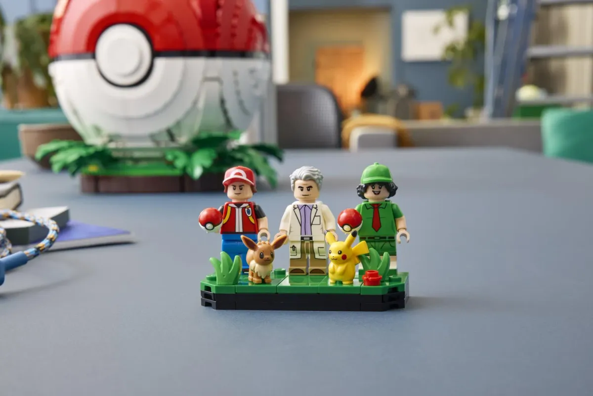 The three LEGO Pokémon minifigures Red, Professor Oak and Picnicker on a grass display base with Pikachu and Eevee figures, the Poké Ball set behind them