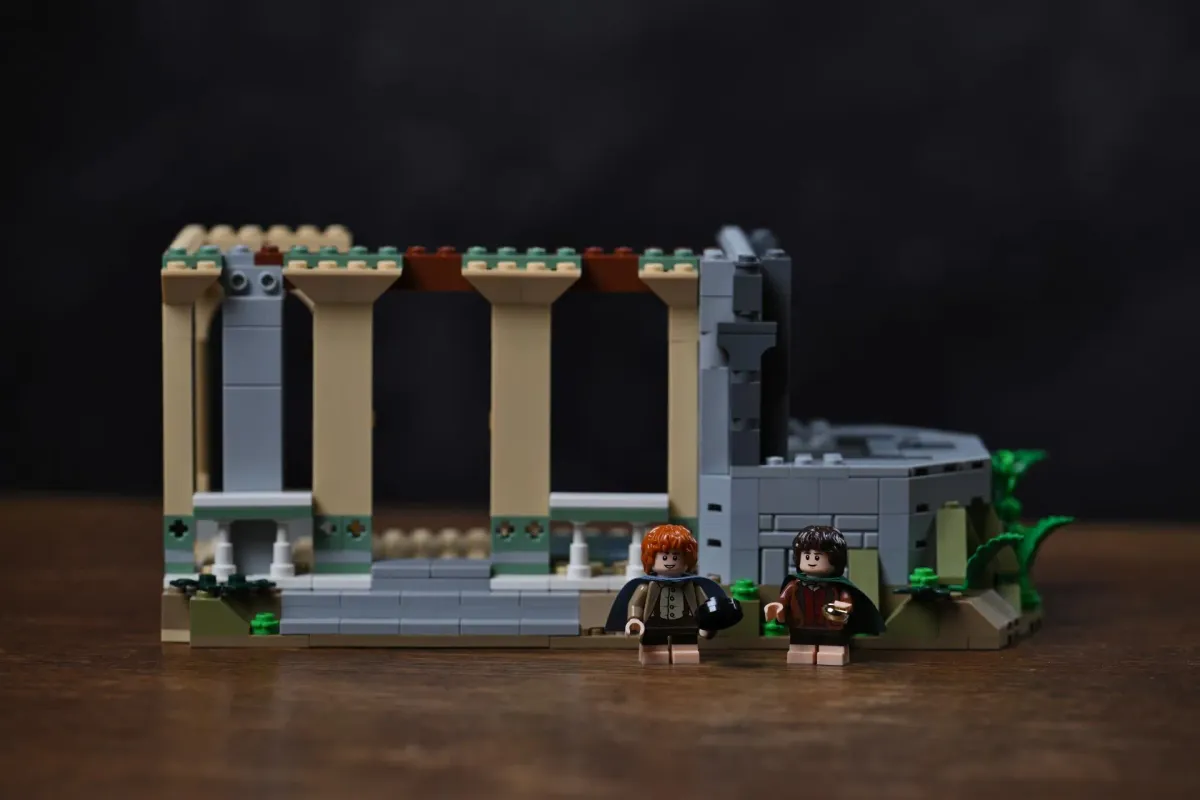A finished early section of the LEGO Rivendell (10316) build displayed on a wooden table, with the Frodo and Sam minifigures standing in front of it