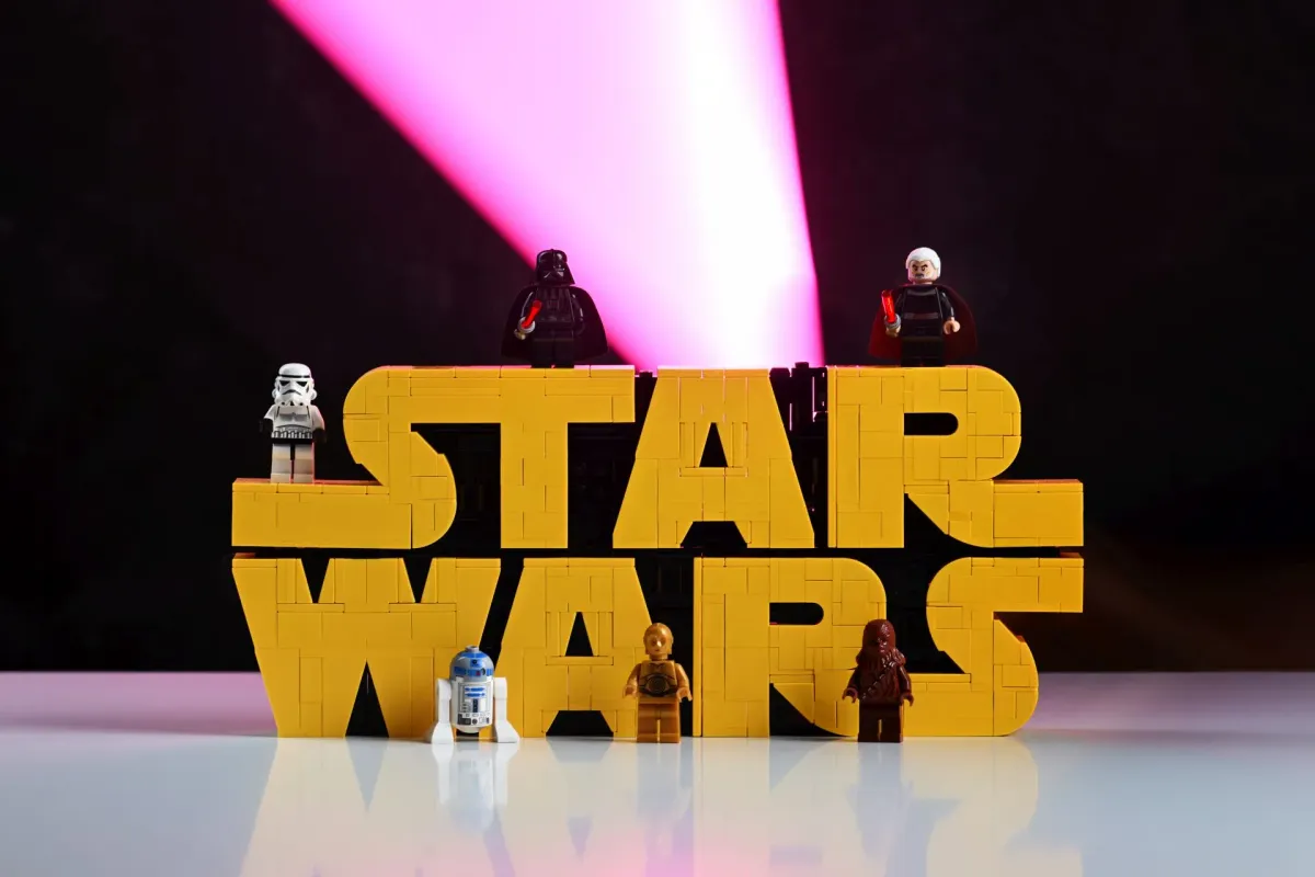 Darth Vader, a Stormtrooper, Count Dooku, R2-D2, C-3PO and Chewbacca minifigures posed on and around the LEGO Star Wars Brick-Built Logo (75407) with dramatic lighting