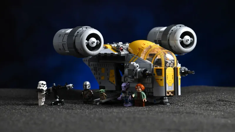 The finished LEGO Star Wars Razor Crest (75447) with all five minifigures - the Mandalorian, Grogu, Colonel Ward, a Remnant Stormtrooper and Zeb Orrelios - lined up in front of the ship