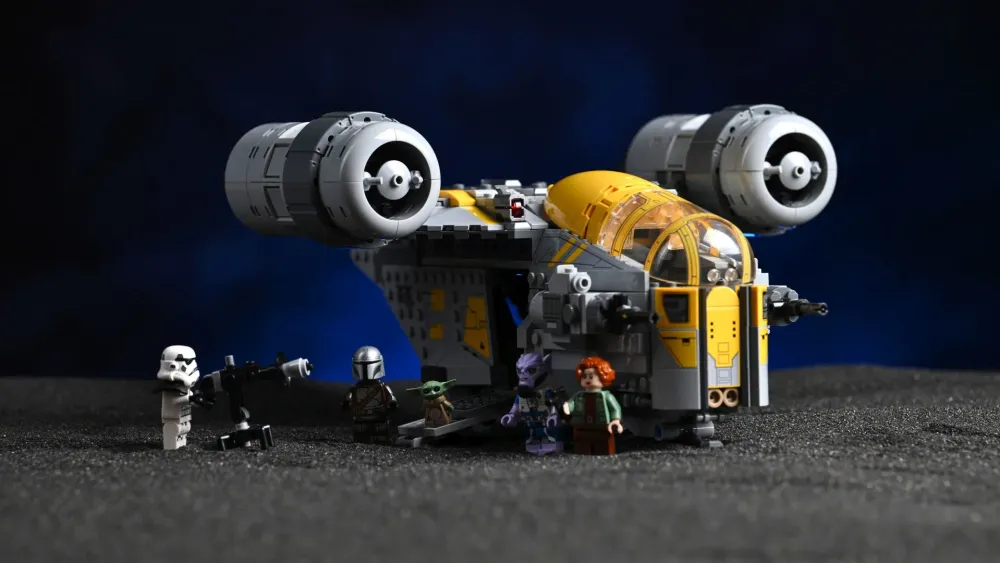 The finished LEGO Star Wars Razor Crest (75447) with all five minifigures - the Mandalorian, Grogu, Colonel Ward, a Remnant Stormtrooper and Zeb Orrelios - lined up in front of the ship