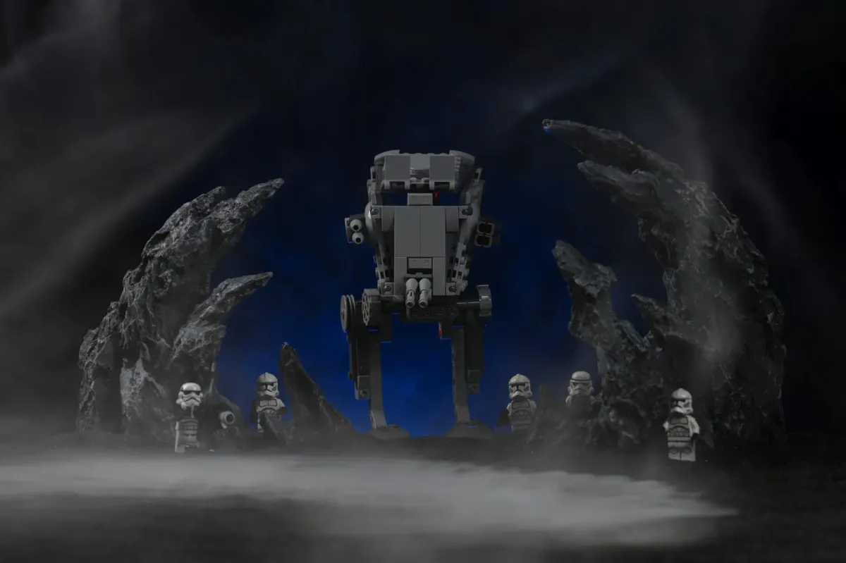 A LEGO AT-ST walker photographed head-on between two jagged rock formations, with soft blue-lit fog drifting through the scene