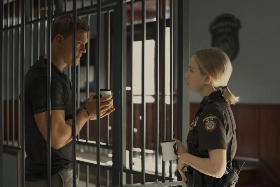 Jack Reacher holds a paper coffee cup inside a Margrave police holding cell, talking through the bars to a uniformed officer
