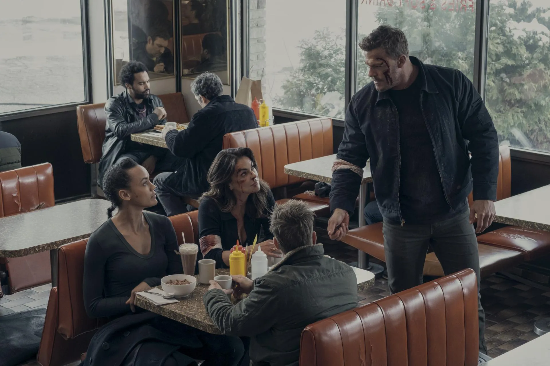 Jack Reacher standing over Frances Neagley, Karla Dixon and David O'Donnell in a diner booth as the 110th reunites in Reacher season 2
