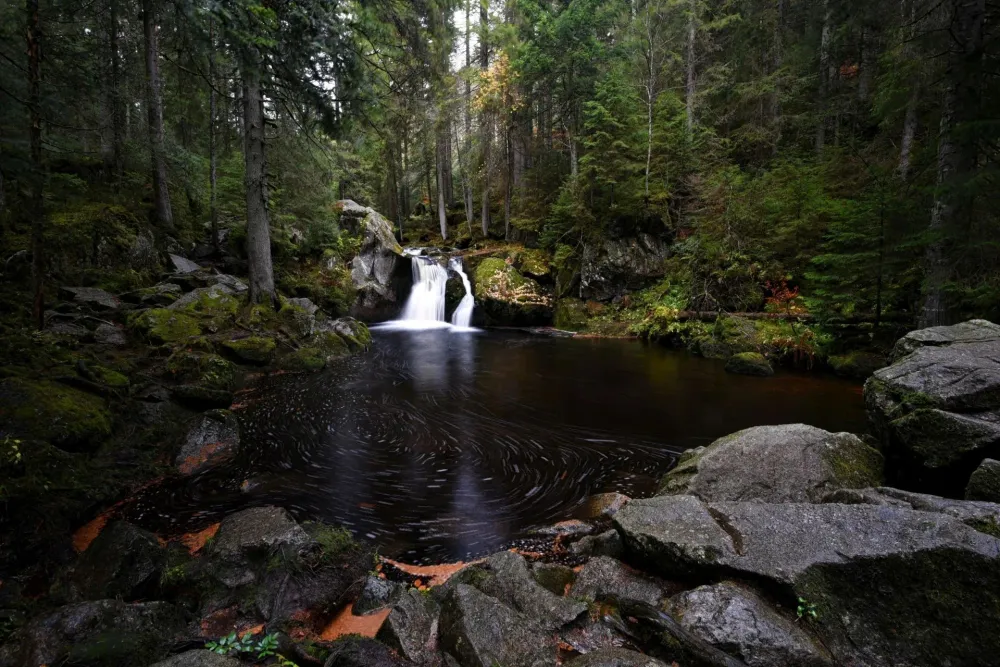 A Black Forest waterfall smoothed to silk by a long exposure, cascading over moss-covered rocks between two dark boulders