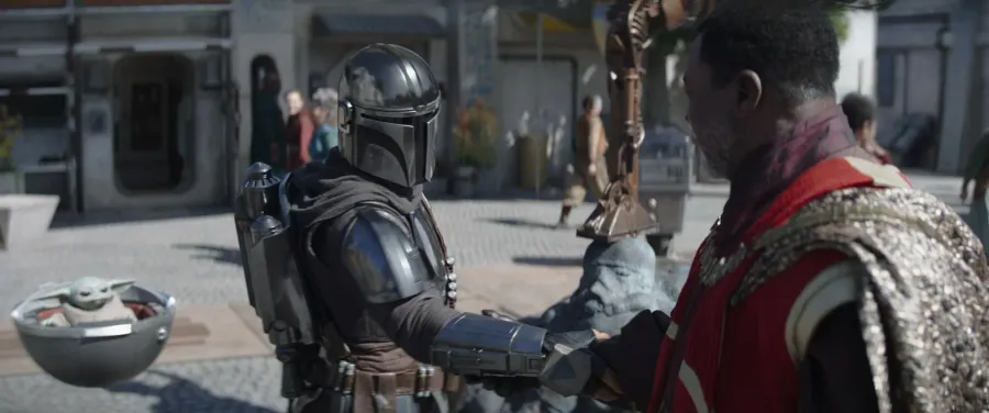 Grogu peering out from between Din Djarin's shoulder and his helmet in The Mandalorian Season 3