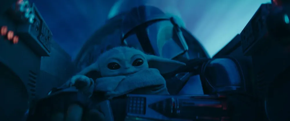 Din Djarin shaking hands with a New Republic official on a city street, with Grogu waiting in his floating cradle, in The Mandalorian Season 3