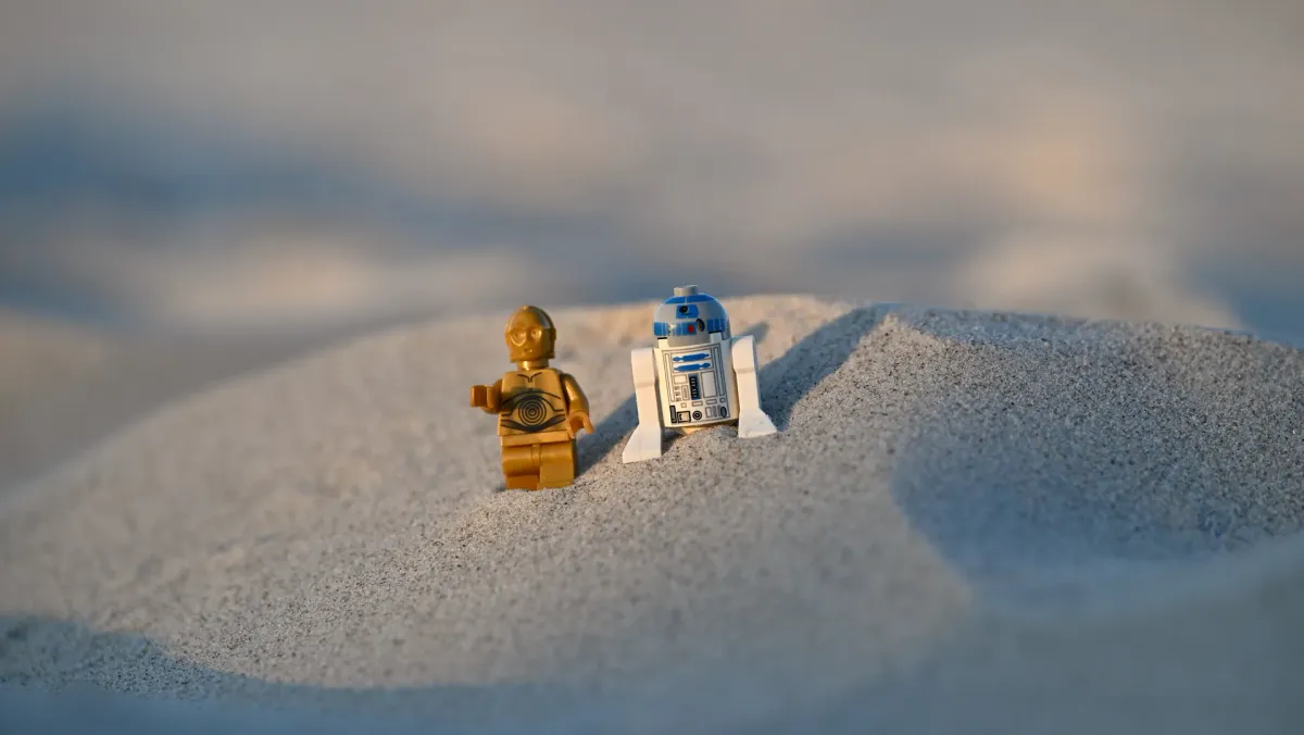 LEGO C-3PO and R2-D2 minifigures walking across expansive sand dunes under soft natural light