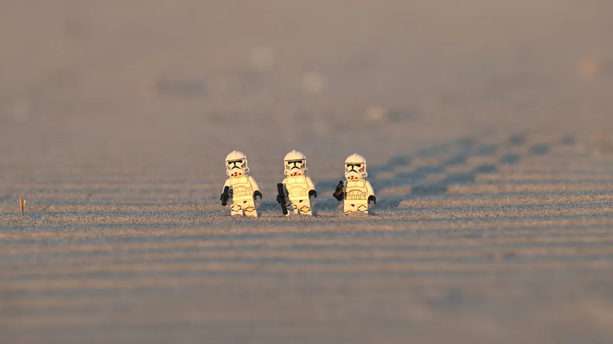 A squad of three LEGO Clone Troopers marching along a wind-carved sand ripple ridge