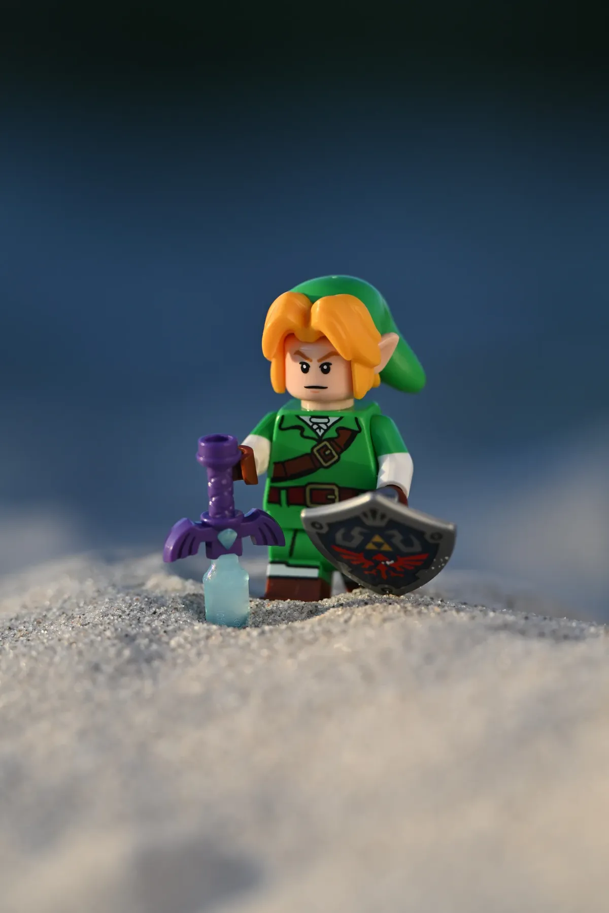 LEGO Link kneeling in a sand dune with the Master Sword planted beside him
